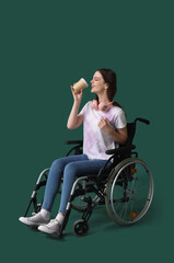 Young woman in wheelchair with cup of coffee on green background