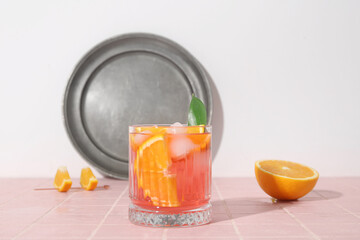 Glass of cold Negroni cocktail and orange on color tile table against light background
