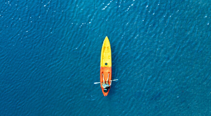 Top view of a woman paddling a yellow and orange kayak on the surface water blue sea. Woman doing...