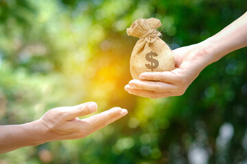 Woman holds a bag of money to a man on a natural green bokeh background. Money saving concept and...