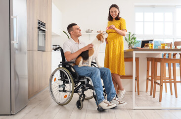 Young man in wheelchair with Beagle dog and his pregnant wife at home