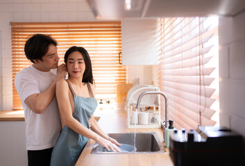 Young Asian couple washing dishes together in the kitchen at home