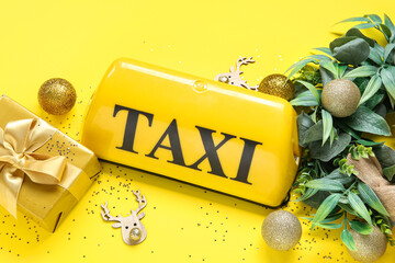Composition with taxi roof sign, gift box and Christmas decorations on yellow background - obrazy, fototapety, plakaty
