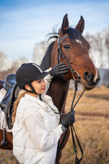 Pretty blond professional female jockey standing near horse. Friendship with horse