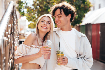 Young smiling beautiful woman and her handsome boyfriend in casual summer clothes. Happy cheerful family. Female having fun. Couple posing in street. Holding and drinking cocktail drink in plastic cup