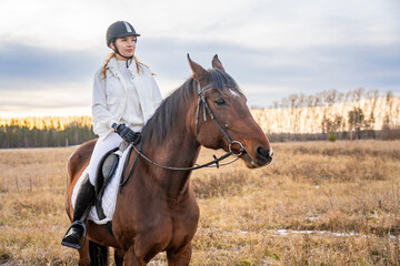Fototapeta premium Beautiful blond professional female jockey riding a horse in field in winter