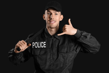 Young police officer with baton showing "call me" gesture on dark background