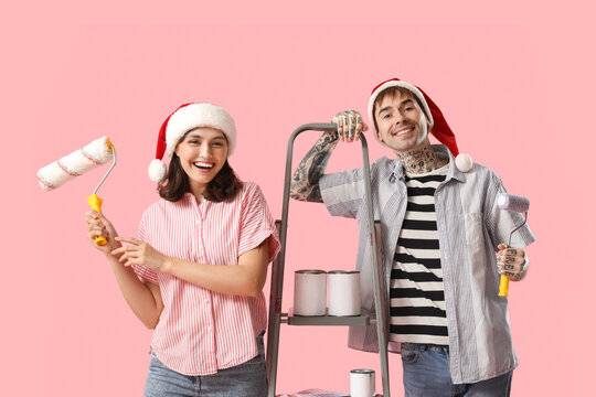 Young couple in Santa hats with painting tools on pink background
