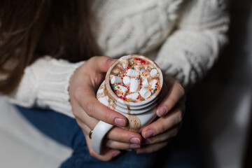 Woman wearing knitted sweater holding tasty cocoa with marshmallow in cup