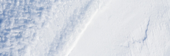 Beautiful winter background with snowy ground. Natural snow texture. Wind sculpted patterns on snow surface. Wide panoramic texture for background and design.