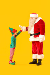 Fototapeta na wymiar Santa Claus and cute little elf on yellow background
