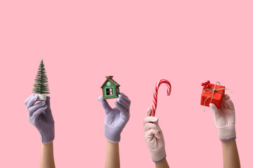 Female hands in warm gloves with Christmas decorations, gift box and candy cane on pink background