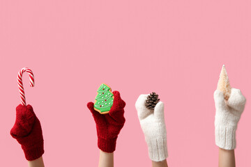 Female hands in warm mittens with Christmas decorations and sweets on pink background
