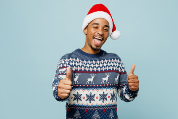 Young smiling cheerful man wear knitted sweater Santa hat posing showing thumb down dislike gesture...