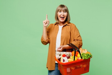 Elderly excited smart happy woman wearing brown shirt casual clothes hold shopping basket bag with...