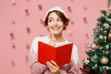Merry young woman wear white sweater hat posing hold in hand notebook write down dreams in diary...