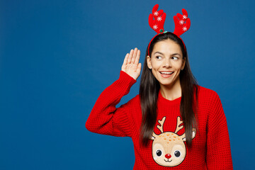 Merry young Latin woman in red Christmas sweater fun decorative deer horns on head posing try to...