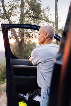 rear view of a woman leaning on the door of her van admiring the landscape in the countryside, concept of adventure travel and active tourism in nature