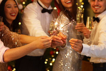 Group of friends with champagne and sparklers celebrating New Year at party, closeup