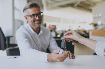 Adult man customer male buyer client wears shirt consult with salesman receive take keys choose auto want buy new automobile in car showroom vehicle salon dealership store motor show. Sales concept.