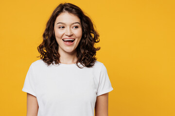 Young surprised happy cheerful fun cool smiling Caucasian woman she wear white blank t-shirt casual clothes looking aside on area mock up isolated on plain yellow orange background. Lifestyle concept.