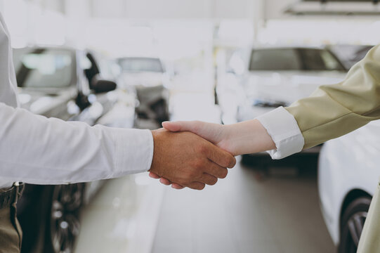 Cropped close up photo of man customer male buyer client shake salesman female hand arm choose auto want to buy new automobile in car showroom vehicle salon dealership store motor show. Sales concept.