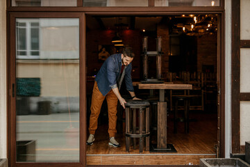 The restaurant owner starts the day early, wiping down tables and setting the scene for a fresh dining experience - obrazy, fototapety, plakaty
