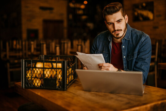 Business-minded restaurateur counting money and updating records on a laptop