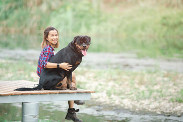 woman and a rottweiler dog on a camping trip in nature. relaxing woman read a book sitting are...
