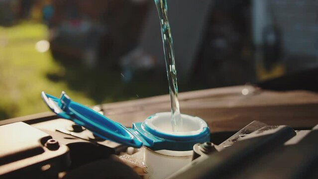 windshield washer fluid is poured into the windshield wiper reservoir of a car, close-up. Slow motion, industry