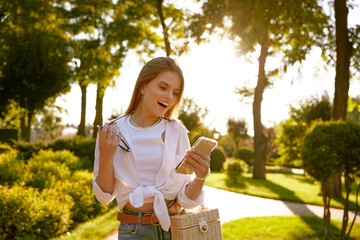 Portrait of young pretty woman with smartphone in park at sunny day