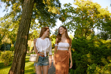 Fototapeta premium Two beautiful young girl friends wearing trendy fashion outfit walking in park