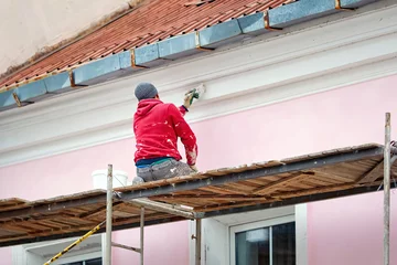 Deurstickers Worker on scaffolding paint facade wall of historic building. Utility worker paints building facade. Repair and restoration building facade. Man painting house wall with paintbrush © Tricky Shark