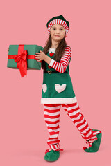 Cute little girl in elf's costume with gift box on pink background
