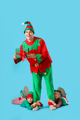 Father and cute little children in elf's costumes with gift box on blue background