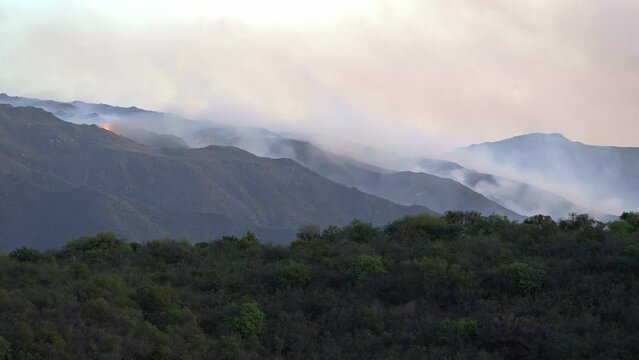 Timelapse of a mountain fire with flames and smoke and forest below in the valley.