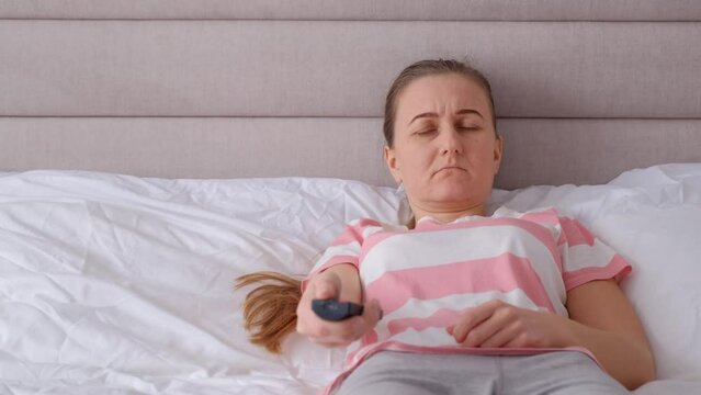 Nervous woman watching TV lying on the bed. Panic attacks in a woman