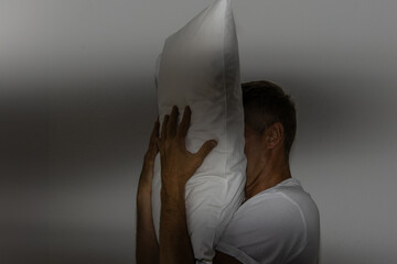Insomnia and man covers his face with pillow.