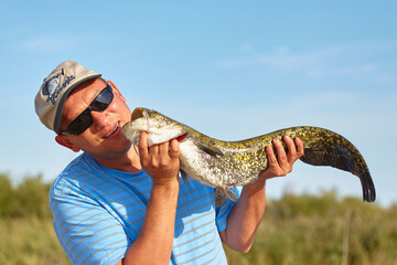 A man on a fishing trip caught a large fish - a lake catfish, and picked it up. Fishing is a great...