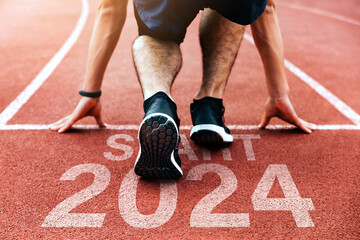 Rear view of a man preparing to start on an athletics track engraved with the year 2024.Happy New Year 2024.challenge, career path and change, readiness of leaders. Goals and plans for the next year.