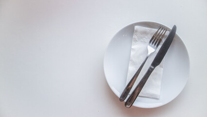 Dinner place setting. White empty plate , silver fork and knife on white background, top view, copy...