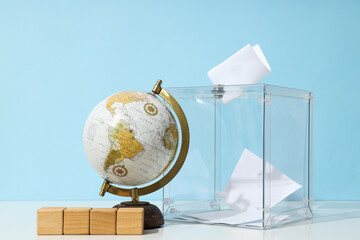 Voting box with papers, wooden cubes and globe on blue background