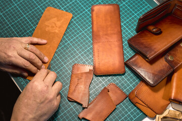 process of making a leather wallet. close up cropped photo. top view. small business. lifestyle. hobby. leather crafting, artisan cuts out patten. old man burnishes the two short edges