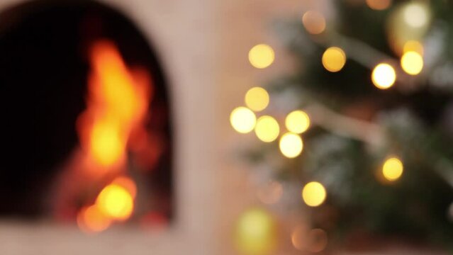 Closeup of blur Christmas tree with garland lights and fireplace with burning fire.