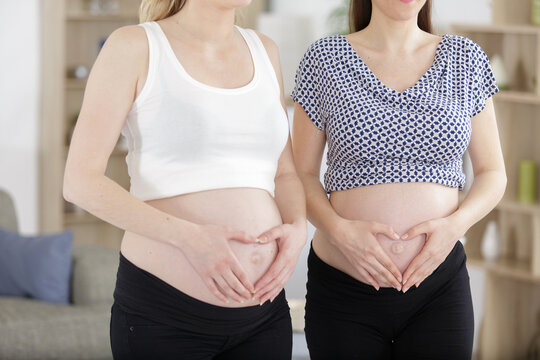 two women making heart shape on their pregnant bellies