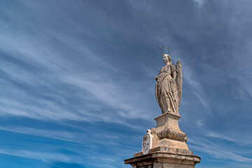 The sculpture of Saint Raphael in the middle of the Roman bridge against the cloudy sky and the ancient city of Córdoba