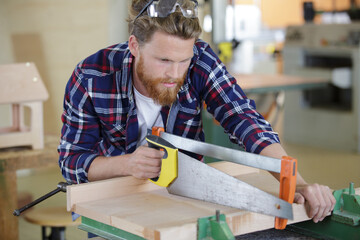 carpenter with saw cutting wooden boards