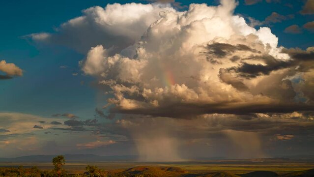 Timelapse of towering cumulus clouds with rain and rainbow at sunset, Hamersley Range, Pilbara, Western Australia.