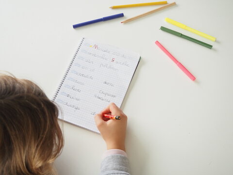 Ni&ntilde;a escribiendo palabras con l&aacute;piz en mesa blanca y rotuladores de colores 