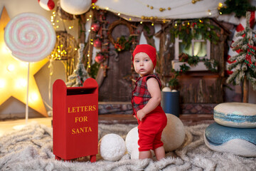 A baby in a checkered vest, a cap and shorts with bare feet in New Year's decorations against the...